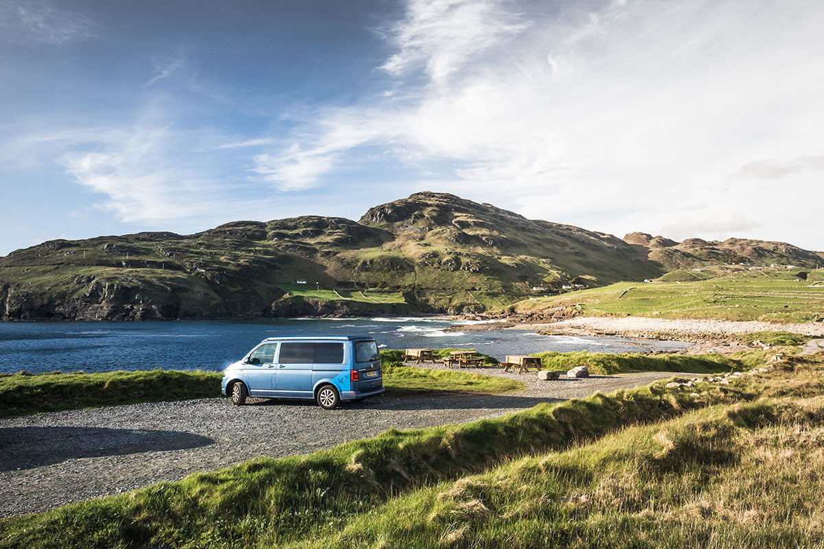 Van parked on a scenic coastal road with mountains in the background